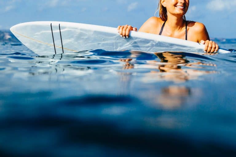 Woman holding on to the rails of her surfboard in the water