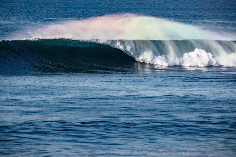 Powerful wave shaped by offshore wind with a rainbow in the sea spray